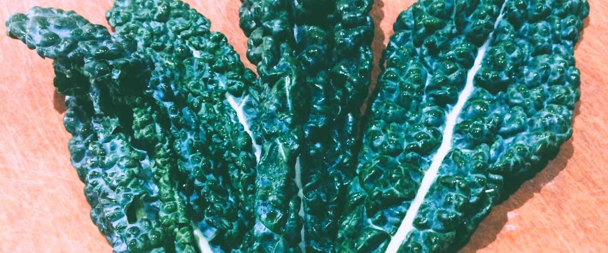 Three leaves of Tuscan kale on a wooden cutting board by Crystal Smith.