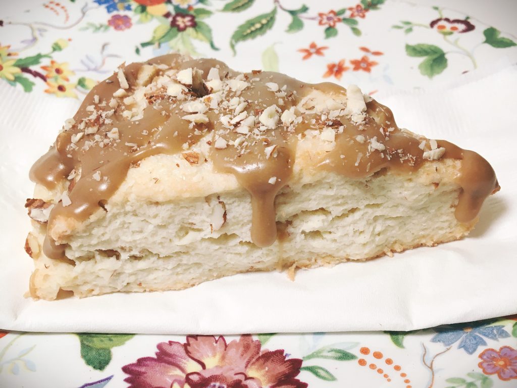 Almond scone with caramel icing on a floral plate.