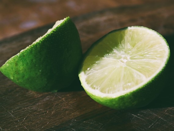 A lime cut in half on a wood cutting board by Emma Miller on Unsplash.