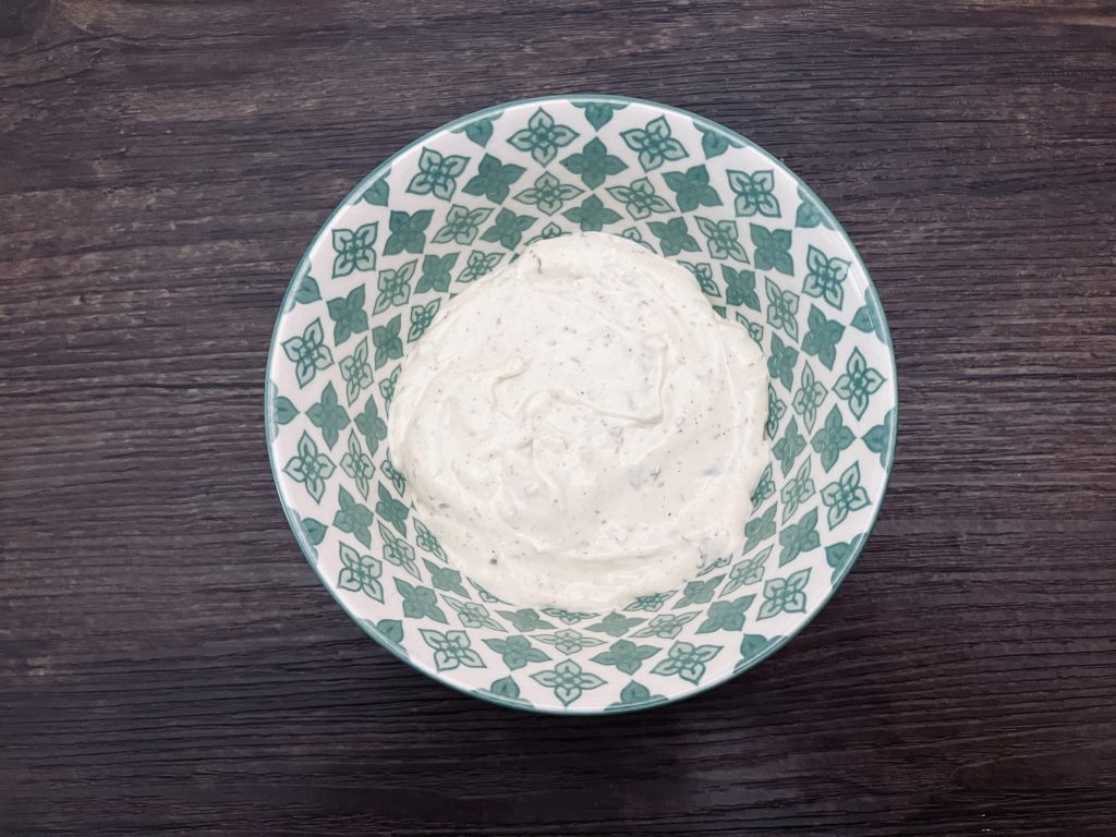 Ranch dressing in a green and white bowl on a wood background.