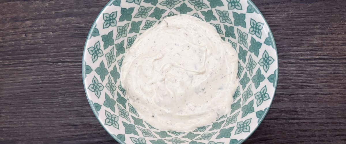 Ranch dressing in a green and white bowl on a wood background.