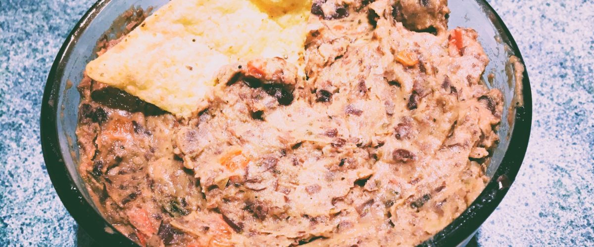 Refried beans in a glass bowl with a tortilla chip dipped in.