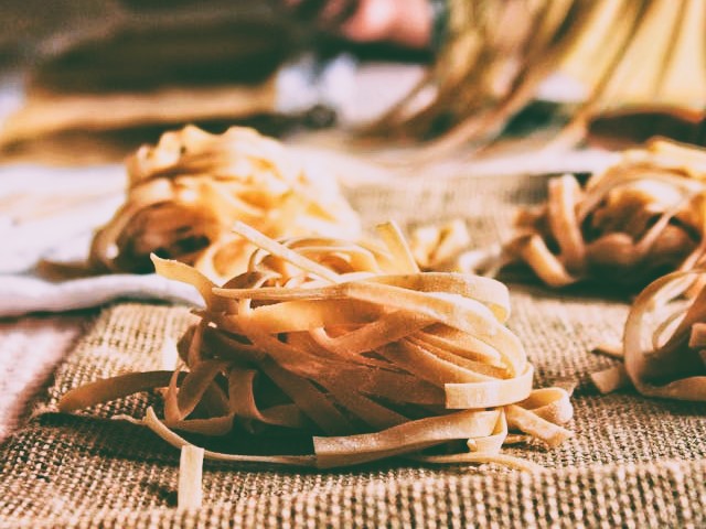 Homemade pasta on burlap with pasta machine in background by Kübra Doğu on Pexels.