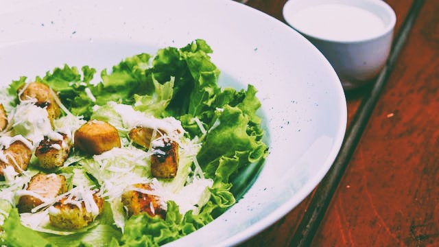Caesar salad in a white bowl on a wood table by Pedro Furtado on Pexels.