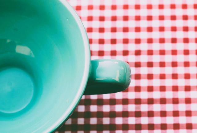 Turquoise coffee mug, closeup, on red gingham background.
